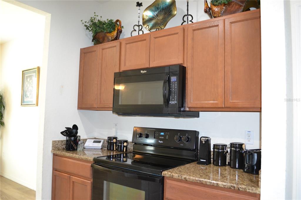A kitchen features wood cabinets, a black microwave, a black stove, and granite countertops — 2828 BLACKWATER CREEK DRIVE, LAKELAND, FL