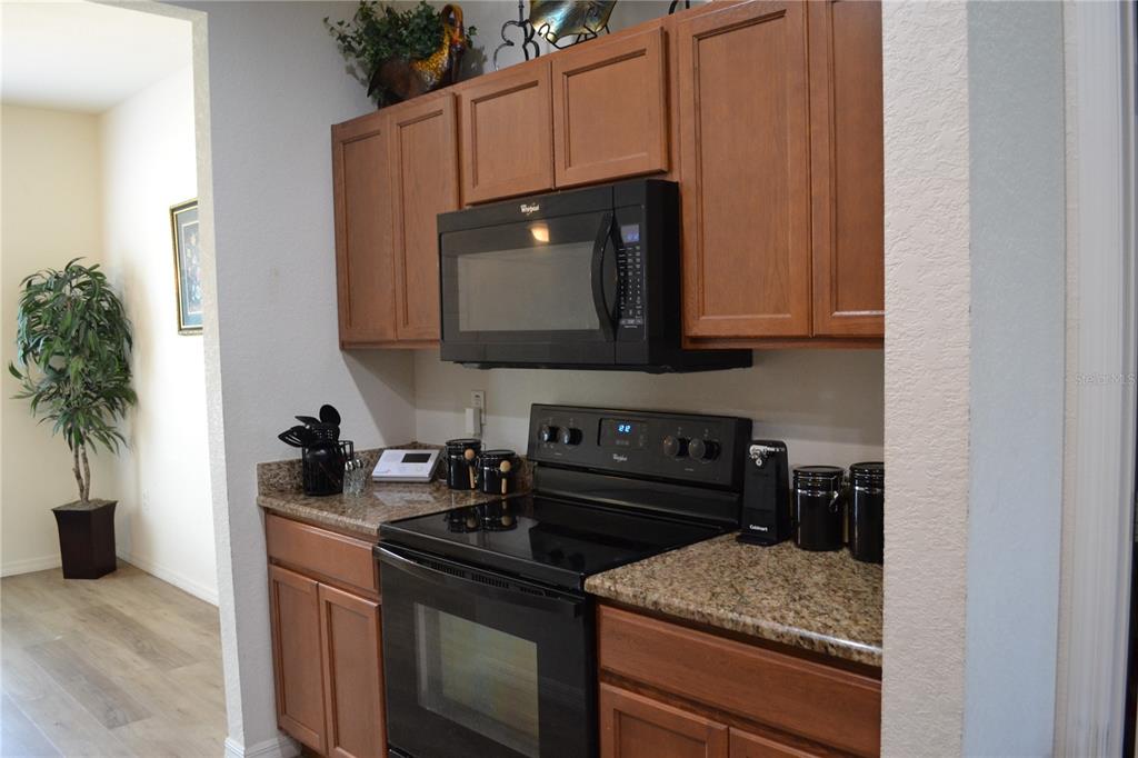 A kitchen features wood cabinets, granite countertops, and black appliances including a microwave and stove — 2828 BLACKWATER CREEK DRIVE, LAKELAND, FL