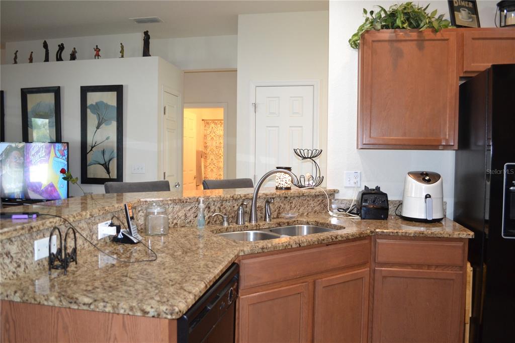 A kitchen features granite countertops, wood cabinets, a double sink, and a black refrigerator — 2828 BLACKWATER CREEK DRIVE, LAKELAND, FL