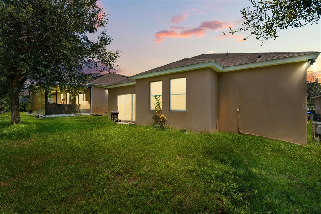 The exterior of a tan house features a grassy backyard, a screened patio, and windows — 1142 GRAND HILLTOP DRIVE, APOPKA, FL