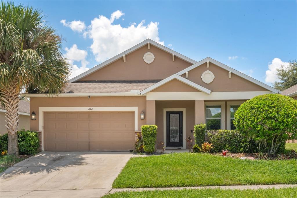 A single-story house with a tan stucco exterior, a two-car garage, and a palm tree — 1142 GRAND HILLTOP DRIVE, APOPKA, FL