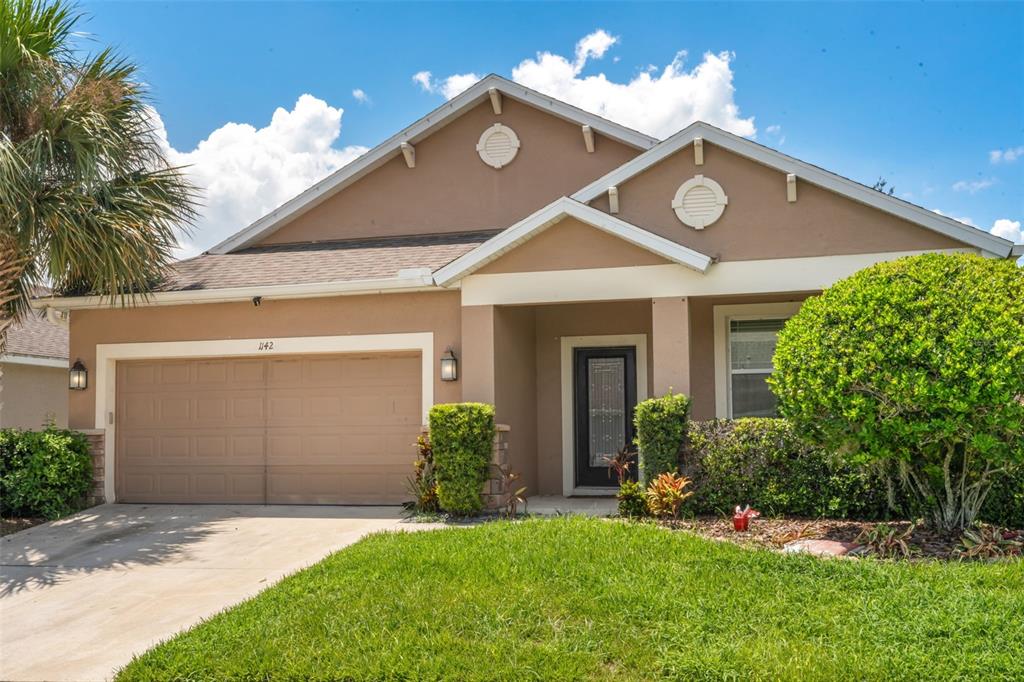 A single-story house with a tan stucco exterior, a two-car garage, and a front lawn — 1142 GRAND HILLTOP DRIVE, APOPKA, FL