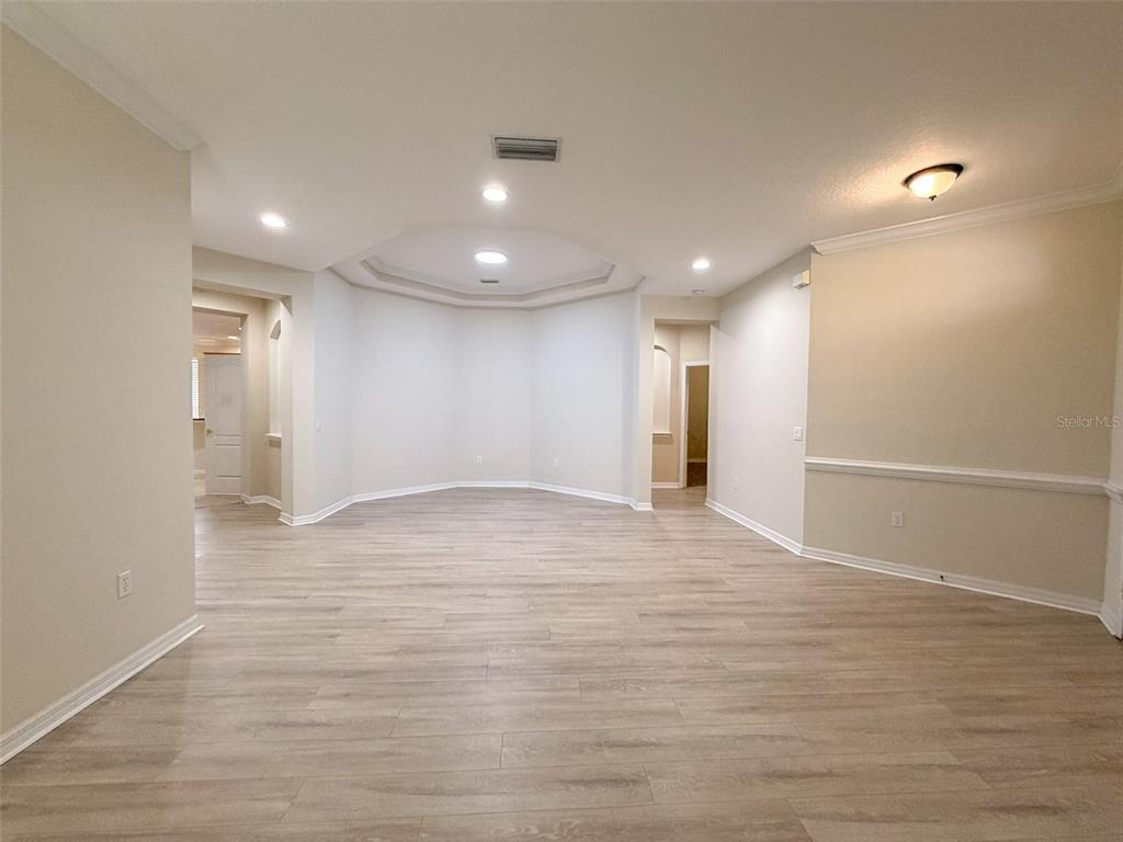 An empty living area features light wood-look flooring, a tray ceiling, and beige walls — 12947 RUNSWICK AVENUE, WINDERMERE, FL