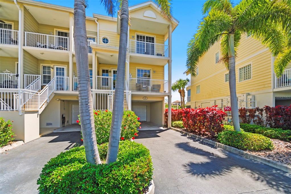 A three-story yellow townhouse with a ground-level garage, balconies, and palm trees in front — 601 BAHIA BEACH BOULEVARD, RUSKIN, FL