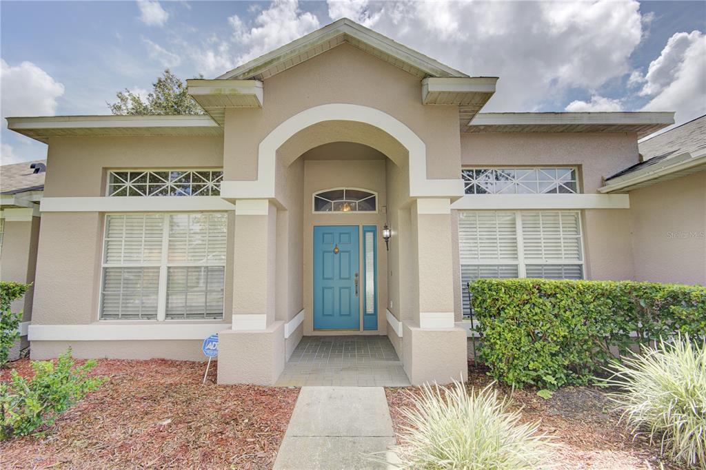 The exterior of a beige house features a bright blue front door and arched entryway — 2688 SUGAR PINE RUN, OVIEDO, FL