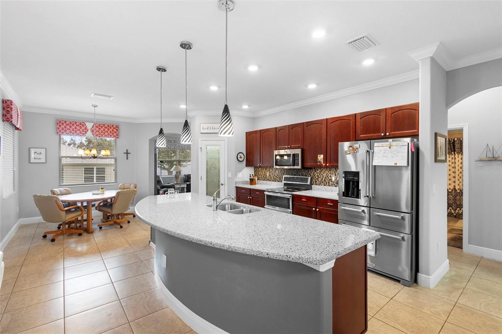 A kitchen features a curved granite island, dark wood cabinets, and an adjacent dining area — 27106 CAMERONS RUN, LEESBURG, FL