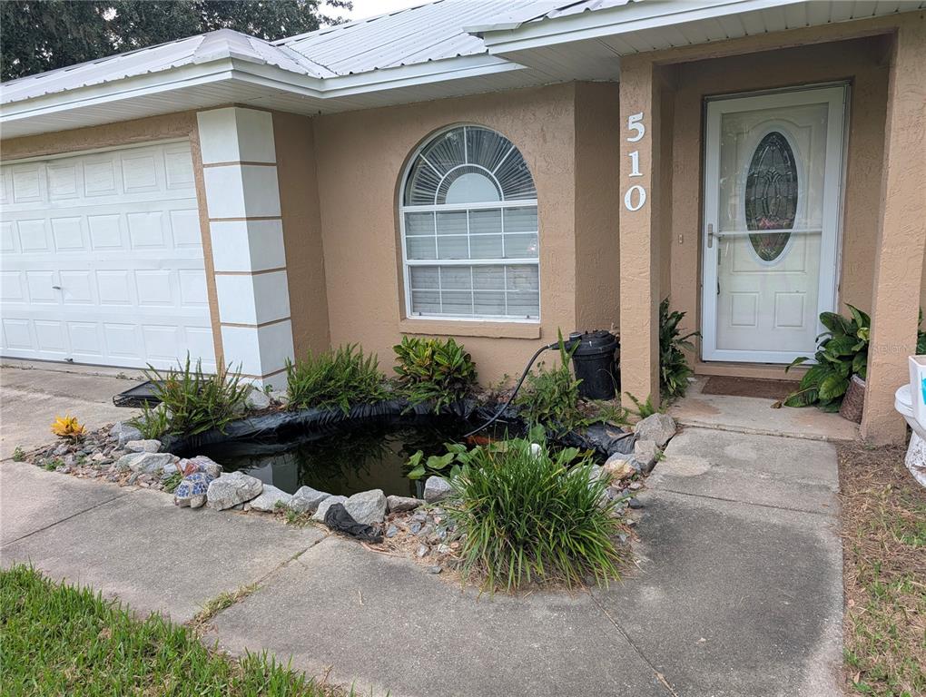A tan house exterior features a front pond, a garage, and a white front door — 510 CLOVERLEAF DRIVE, LITHIA, FL