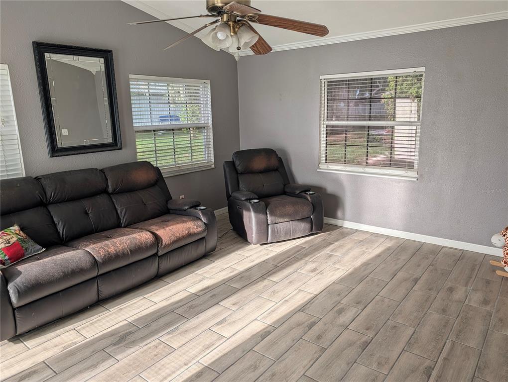 A living room features gray walls, wood-look tile flooring, a leather sofa, and a recliner — 510 CLOVERLEAF DRIVE, LITHIA, FL