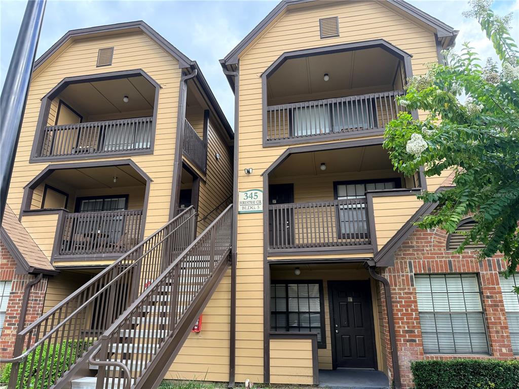 A low-angle exterior view of a three-story apartment building with tan siding and brown balconies — 345 FORESTWAY CIRCLE UNIT 107, ALTAMONTE SPRINGS, FL