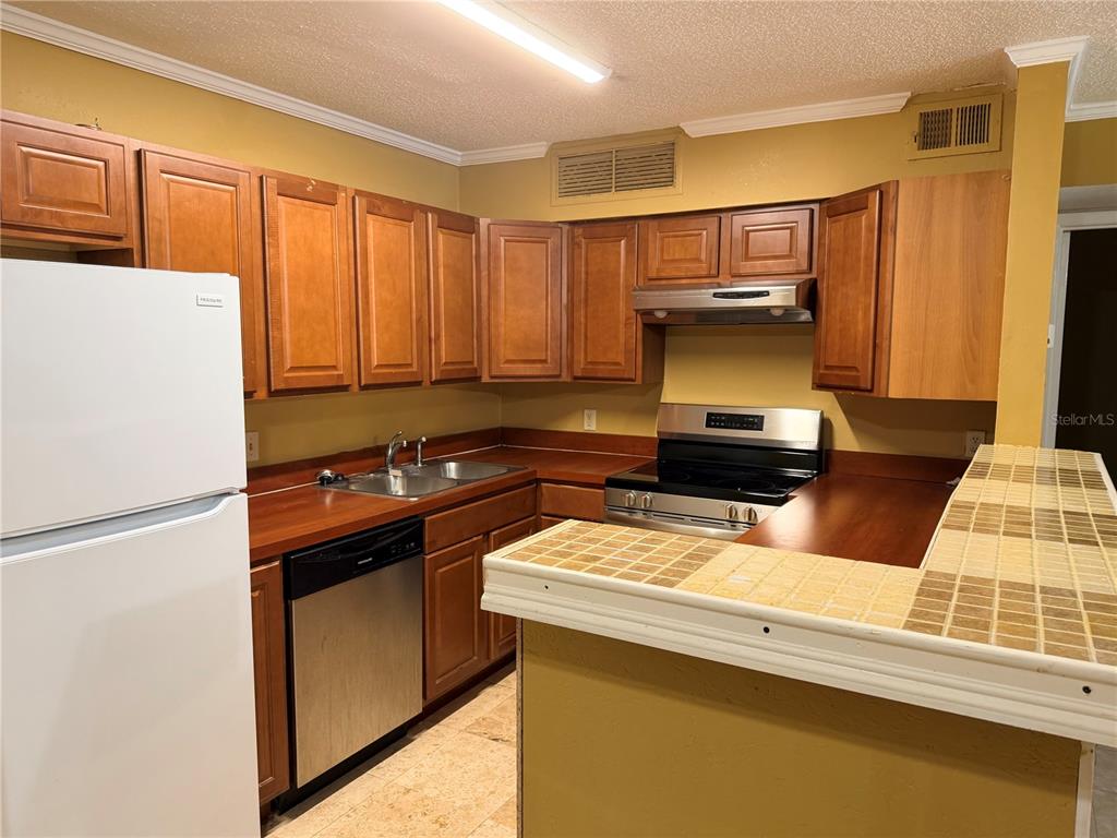 A kitchen features wood cabinets, a white refrigerator, a dishwasher, and a tiled breakfast bar — 345 FORESTWAY CIRCLE UNIT 107, ALTAMONTE SPRINGS, FL