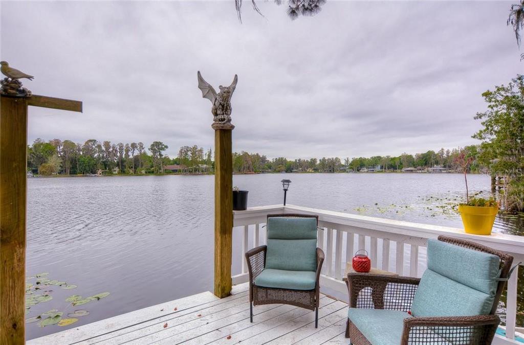 A wooden deck overlooking a lake features two wicker chairs and a decorative gargoyle statue — 20026 HIDEAWAY LANE, LUTZ, FL