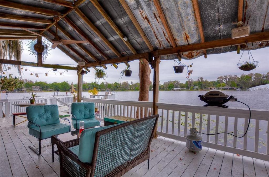 A covered wooden deck overlooks a lake with outdoor furniture and a grill — 20026 HIDEAWAY LANE, LUTZ, FL