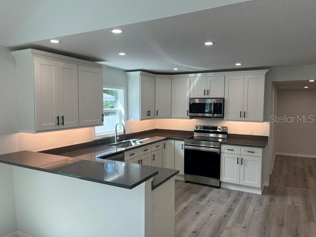 A kitchen features white shaker cabinets, dark countertops, stainless steel appliances, and light wood flooring — 1574 EWING AVENUE, CLEARWATER, FL