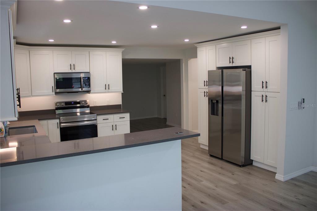 A modern kitchen features white cabinets, stainless steel appliances, and dark gray countertops — 1574 EWING AVENUE, CLEARWATER, FL
