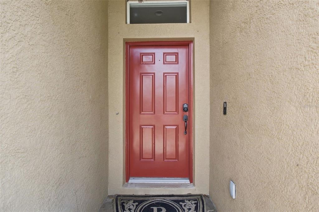 A red front door with a transom window is set within a tan stucco entryway — 9710 WHITE BARN WAY, RIVERVIEW, FL