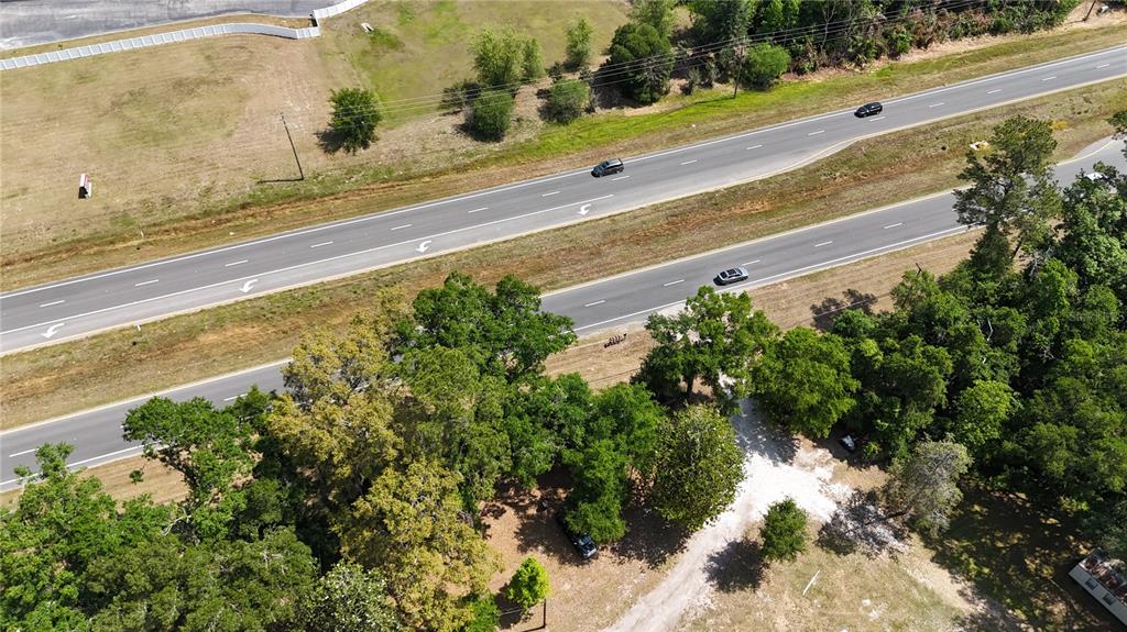 An aerial view shows a multi-lane highway running alongside a wooded area and a dirt driveway — 12100 NW US HIGHWAY 441, GAINESVILLE, FL