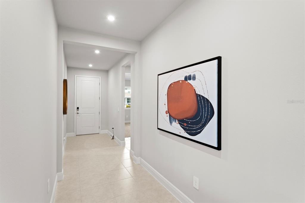 A hallway with light tile flooring, white walls, recessed lighting, and abstract wall art — 35468 PEAK WILLOW TRACE, DADE CITY, FL