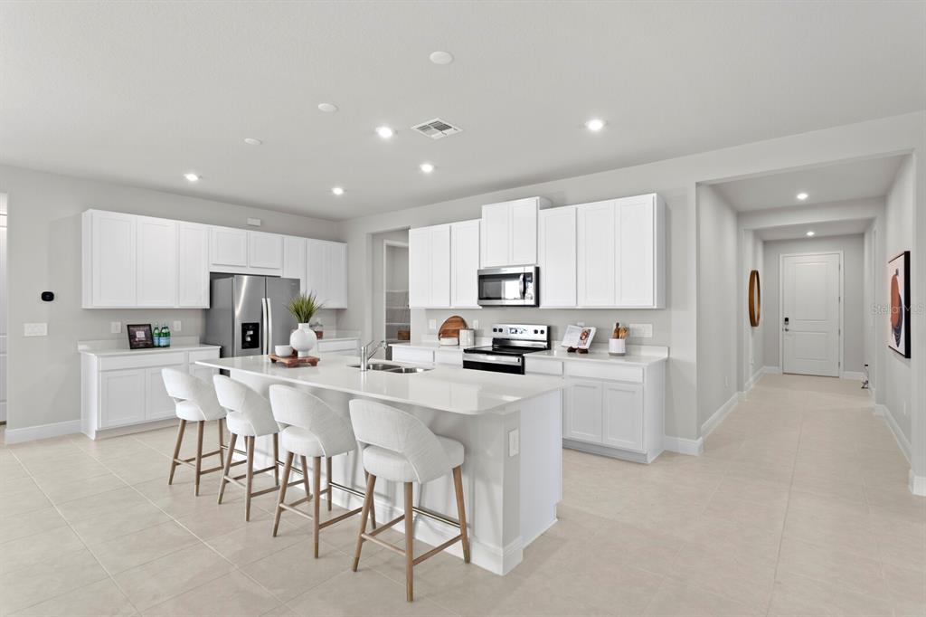 A bright, modern kitchen features white cabinetry, a large island with bar seating, and stainless appliances — 35468 PEAK WILLOW TRACE, DADE CITY, FL