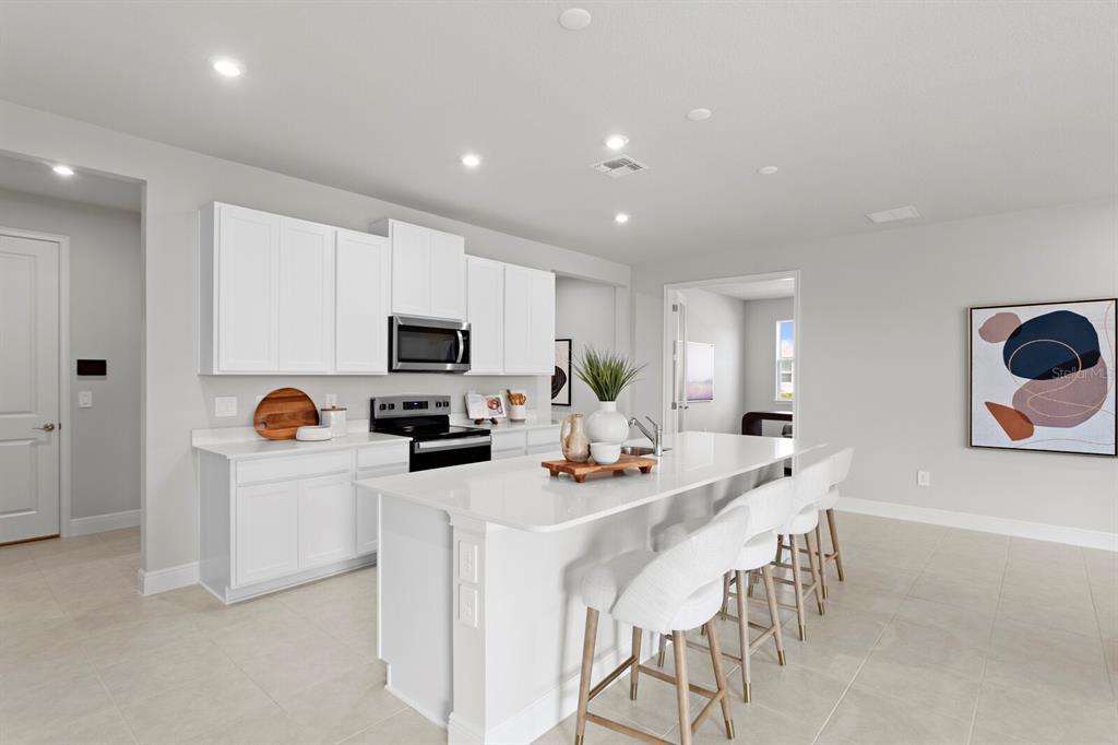 A modern kitchen features white cabinetry, a large quartz island, and light-colored tile flooring — 35468 PEAK WILLOW TRACE, DADE CITY, FL