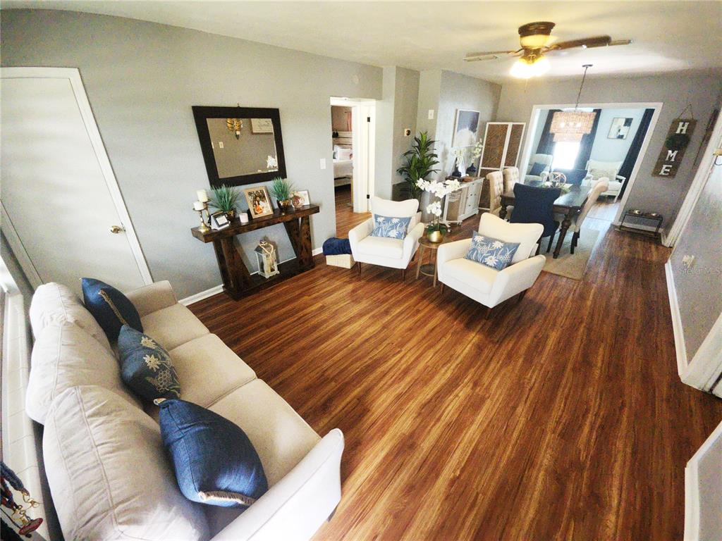 A living room with wood-look flooring, a white sofa, two armchairs, and a dining area — 1337 LEE COURT, LEESBURG, FL