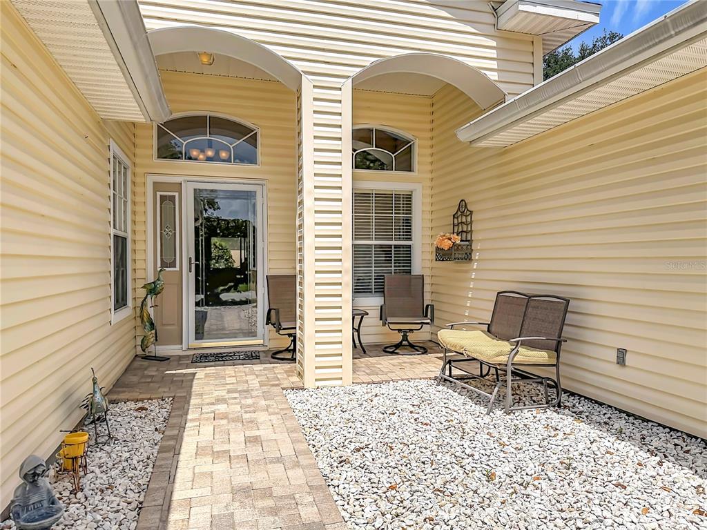 A covered entryway features light yellow siding, a paver walkway, and white gravel landscaping — 25243 RIVER CREST DRIVE, LEESBURG, FL