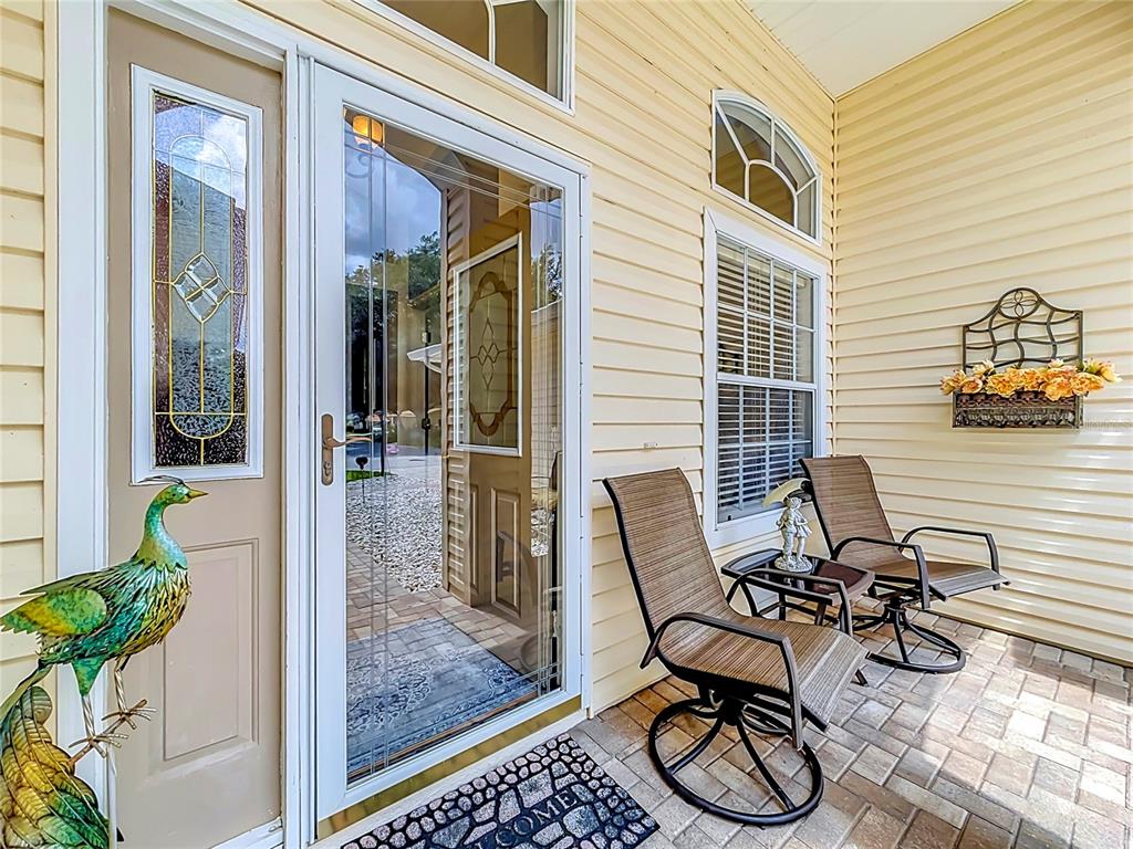 A front porch features a glass storm door, two patio chairs, and a decorative peacock statue — 25243 RIVER CREST DRIVE, LEESBURG, FL