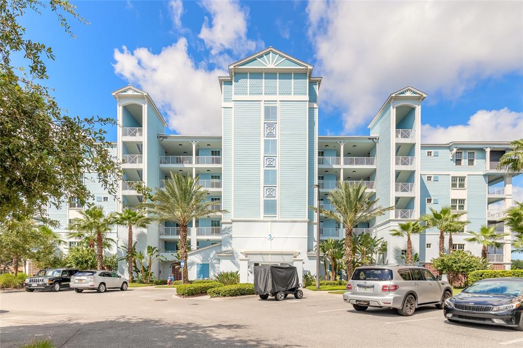 A multi-story light blue residential building with a parking lot in the foreground — 3 RIVERWALK DRIVE UNIT 602, NEW SMYRNA BEACH, FL
