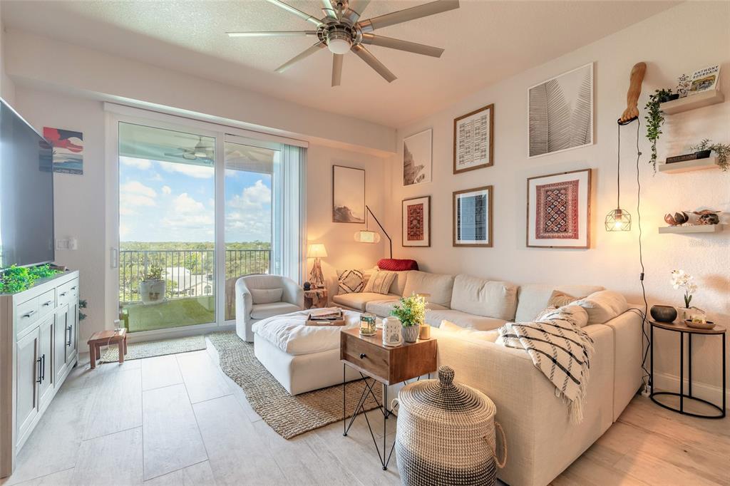 A bright living room features a large sectional sofa, a ceiling fan, and a balcony view — 3 RIVERWALK DRIVE UNIT 602, NEW SMYRNA BEACH, FL