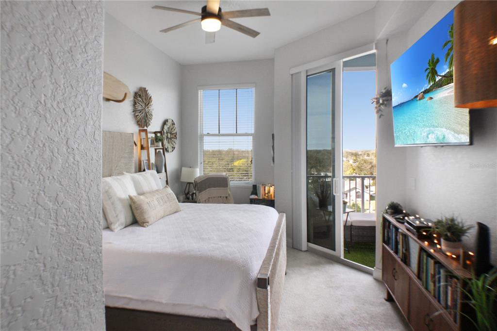A bedroom features a queen bed, a ceiling fan, a wall-mounted television, and a balcony door — 3 RIVERWALK DRIVE UNIT 602, NEW SMYRNA BEACH, FL