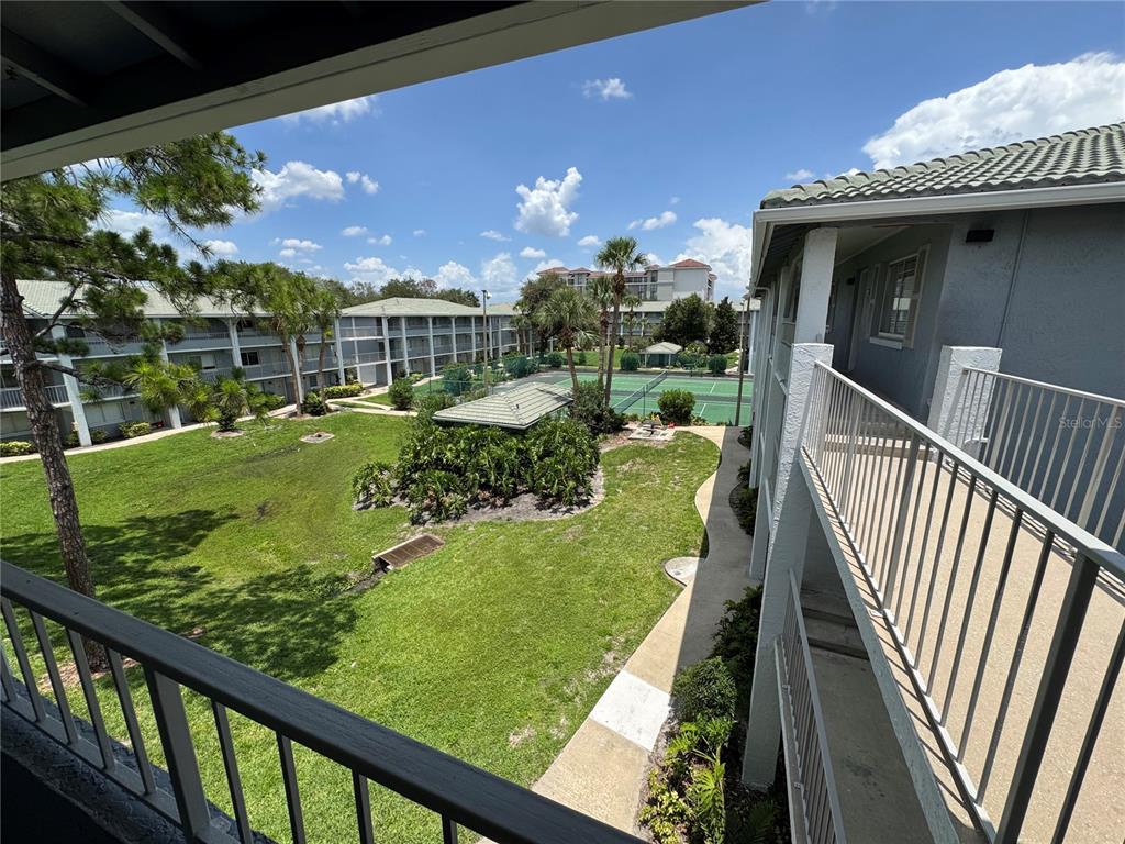 An elevated view from a balcony overlooking a grassy courtyard, tennis courts, and apartment buildings — 115 OYSTER BAY CIRCLE UNIT 300, ALTAMONTE SPRINGS, FL