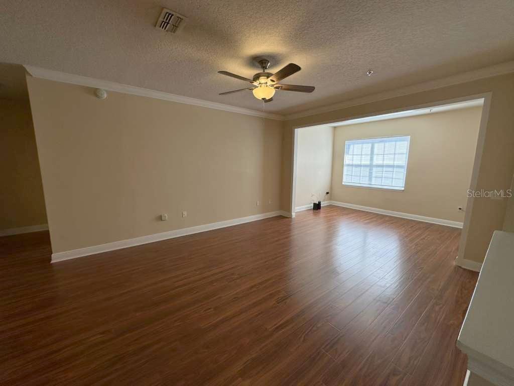 An empty living room features wood-look laminate flooring, a ceiling fan, and a recessed nook — 225 SOUTHERN PECAN CIRCLE UNIT 208, WINTER GARDEN, FL