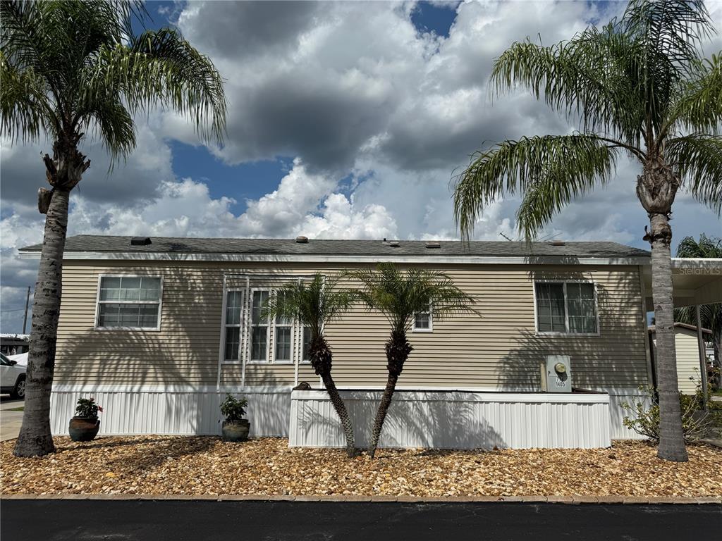 A single-story manufactured home with beige siding, white skirting, and several palm trees in front — 1405 STARBOARD DRIVE, ST CLOUD, FL