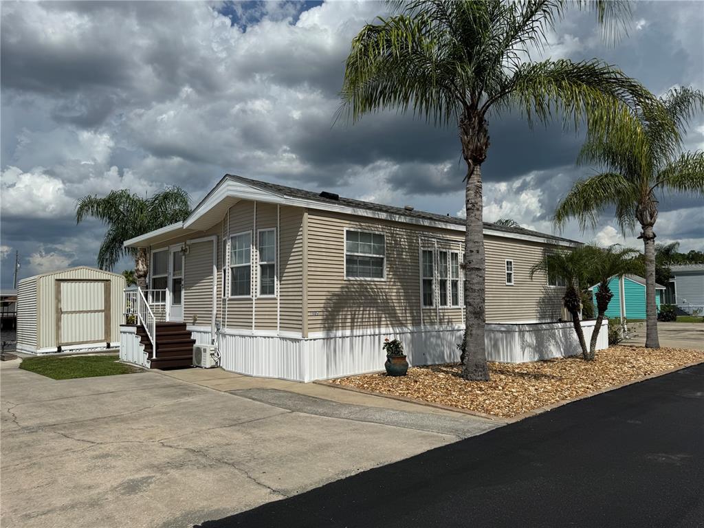 A tan mobile home with white skirting, a small storage shed, and palm trees outside — 1405 STARBOARD DRIVE, ST CLOUD, FL