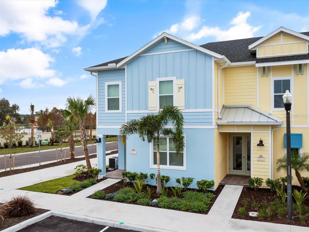 A two-story duplex with blue and yellow siding, palm trees, and concrete walkways — 8217 SURF STREET, KISSIMMEE, FL