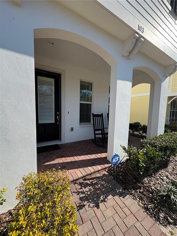 A covered brick porch features a dark front door and two rocking chairs — 103 CUTLASS WAY, OLDSMAR, FL