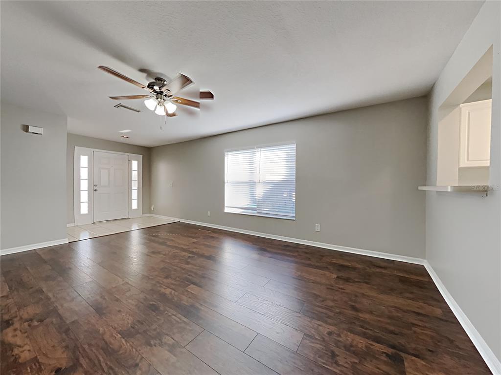 An empty living room features dark wood-look flooring, light gray walls, and a ceiling fan — 404 SUMMER SAILS DRIVE, VALRICO, FL