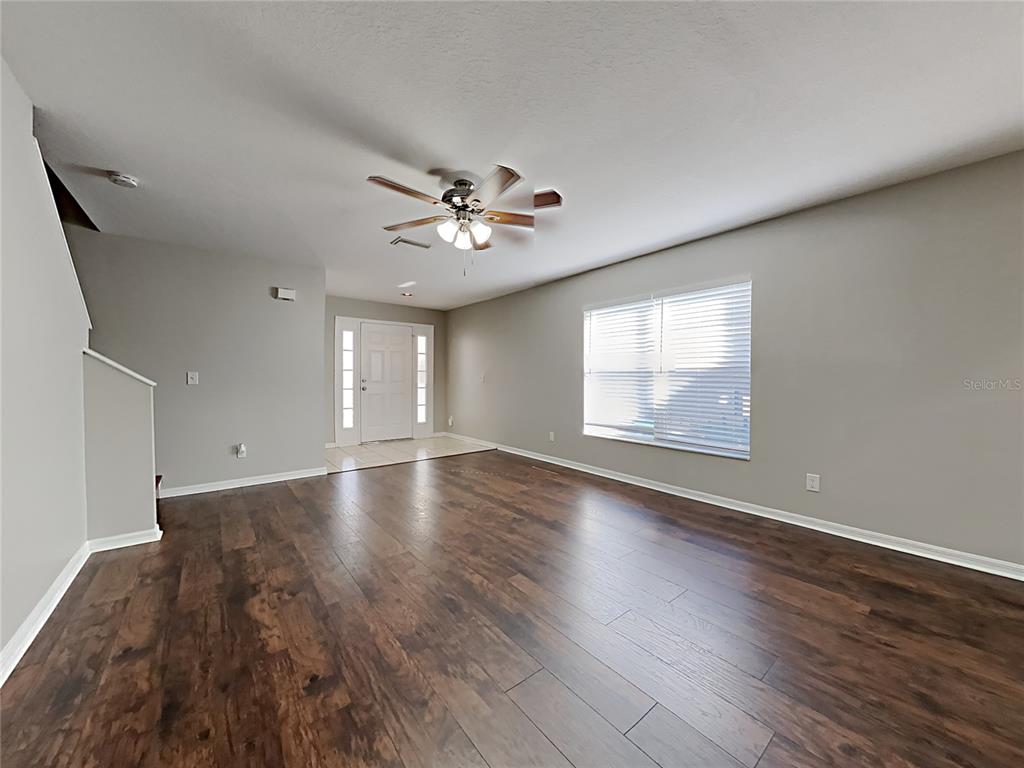 An empty living room features dark wood-look flooring, light gray walls, and a ceiling fan — 404 SUMMER SAILS DRIVE, VALRICO, FL