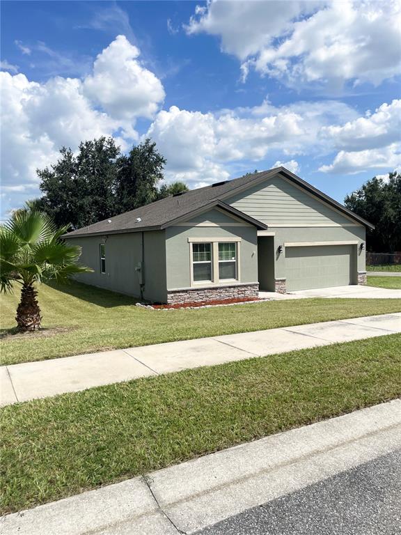 A single-story house with a green stucco exterior, stone accents, and an attached two-car garage — 15725 PINE SISKIN LOOP, MASCOTTE, FL