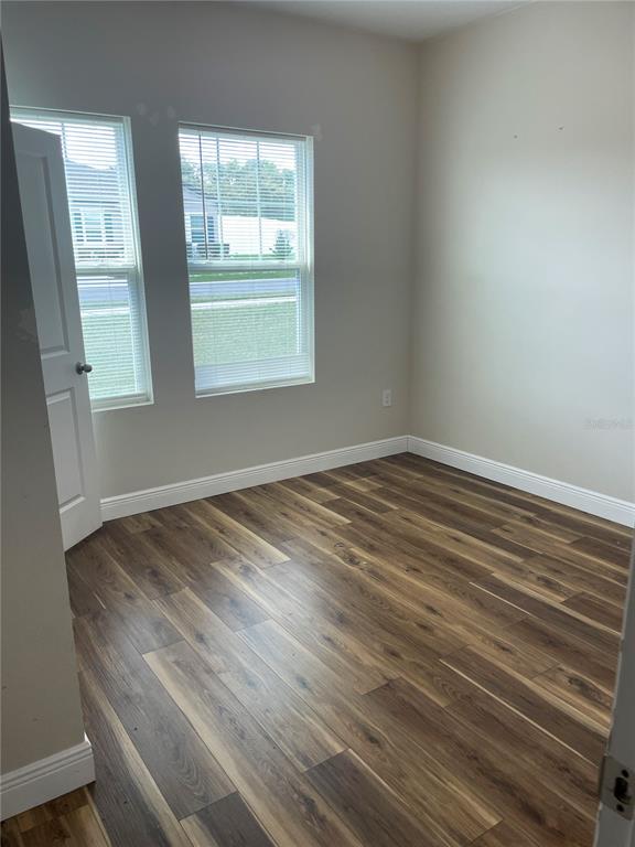 An empty room features wood-look flooring, two windows with blinds, and a white door — 15725 PINE SISKIN LOOP, MASCOTTE, FL