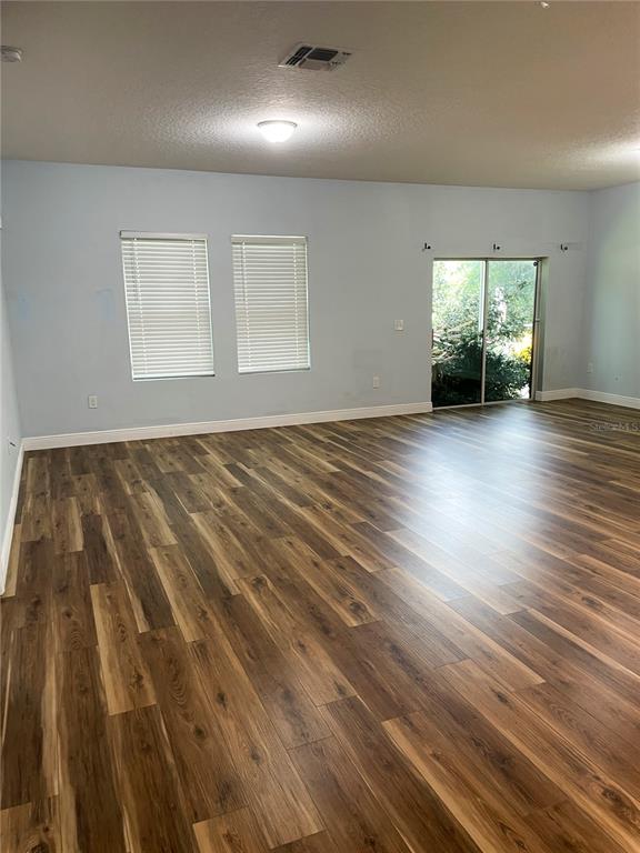An empty room features light blue walls, wood-look flooring, two windows with blinds, and sliding doors — 15725 PINE SISKIN LOOP, MASCOTTE, FL