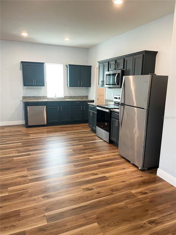 A kitchen features dark cabinets, stainless steel appliances, granite countertops, and wood-look flooring — 15725 PINE SISKIN LOOP, MASCOTTE, FL