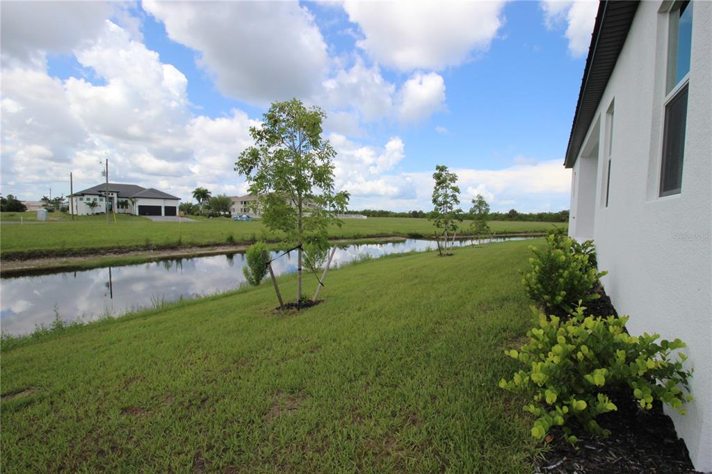 A view of a grassy backyard with a small canal, young trees, and a house exterior — 17030 ESPANA CIRCLE, PUNTA GORDA, FL