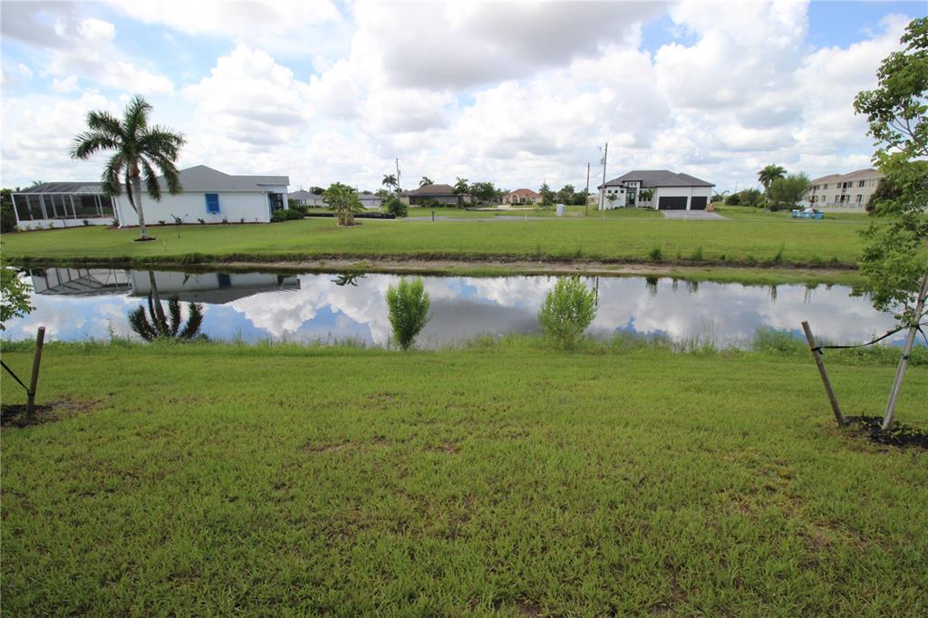 A grassy backyard overlooks a canal with houses in the background under a cloudy sky — 17030 ESPANA CIRCLE, PUNTA GORDA, FL