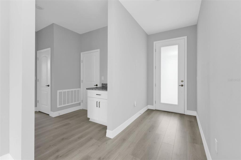 A hallway with light gray walls, wood-look flooring, a white door, and a small cabinet — 17030 ESPANA CIRCLE, PUNTA GORDA, FL