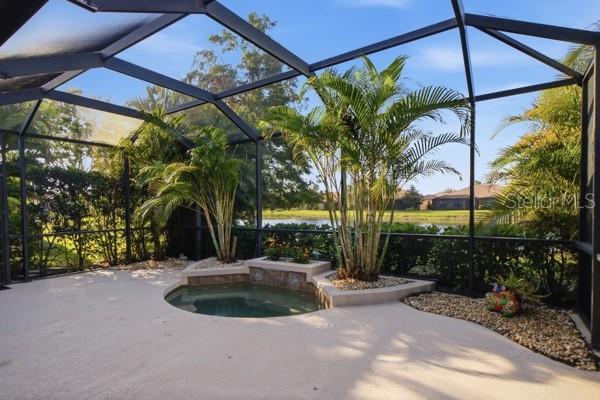 A screened-in patio features a small built-in spa, palm trees, and a view of water — 1884 BATELLO DRIVE, VENICE, FL