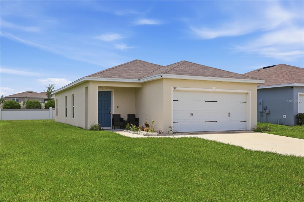 A single-story house with a beige exterior, a two-car garage, and a dark front door — 1403 MADISON CIRCLE, HAINES CITY, FL
