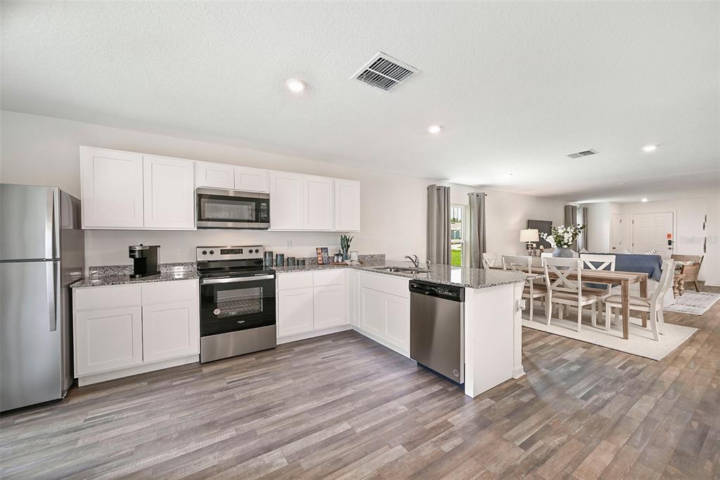 A kitchen with white cabinets, granite countertops, and a breakfast bar with three stools — 1745 EAGLE HAMMOCK BOULEVARD, EAGLE LAKE, FL