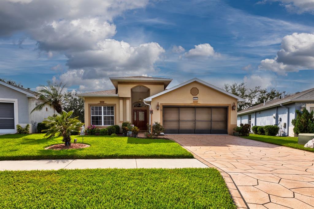 A single-story suburban house with a tan stucco exterior, a two-car garage, and a driveway — 5615 CELEBRATION WAY, LEESBURG, FL