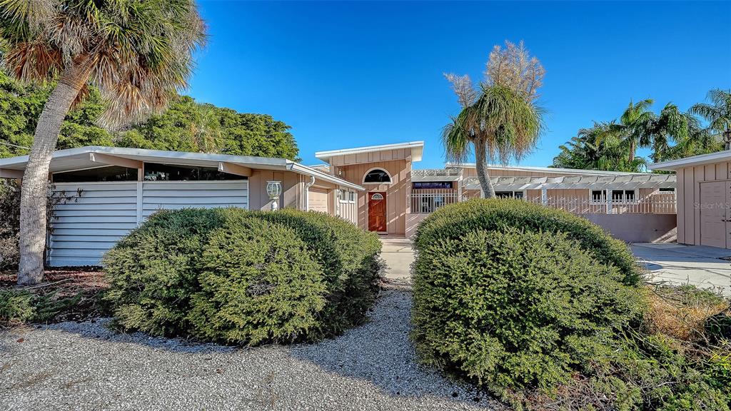 A single-story house with a flat roof, wood siding, and large bushes in the front — 355 S SHORE DRIVE, SARASOTA, FL