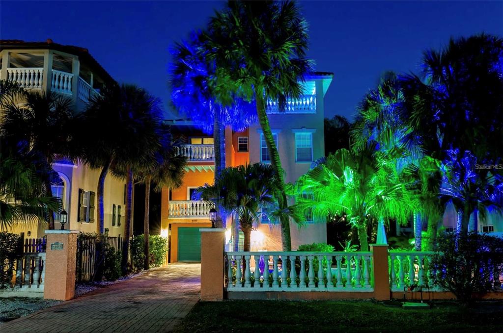 A multi-story house at night with palm trees illuminated by blue and green landscape lighting — 4003 5TH AVENUE, HOLMES BEACH, FL